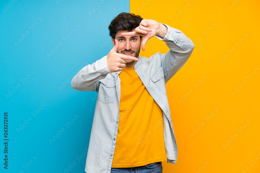 Handsome over isolated colorful background focusing face. Framing symbol Handsome over isolated colorful background focusing face. Framing symbol