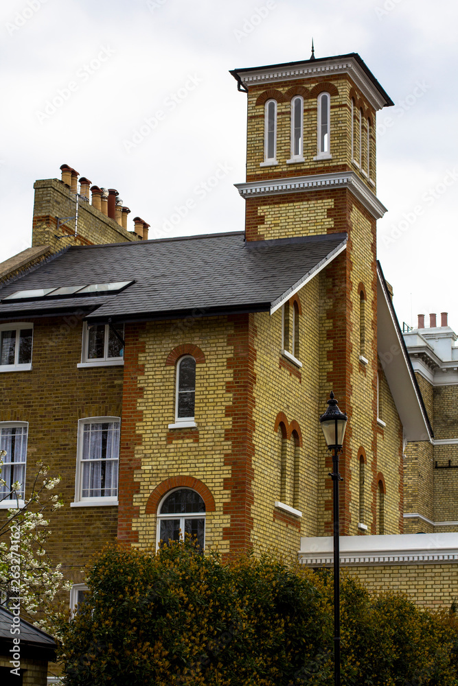 Brick house with white windows and a tower in a quiet area of central London. Lamppost, flowering trees. Brick house with white windows and a tower in a quiet area of central London. Lamppost, flowering trees.