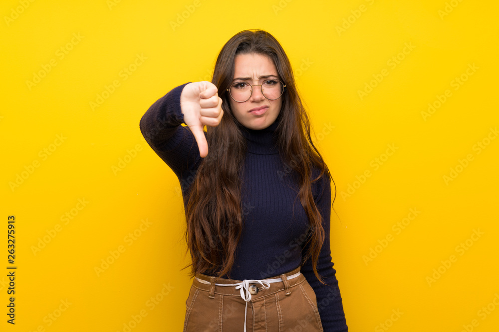 Teenager girl over isolated yellow wall showing thumb down with negative expression Teenager girl over isolated yellow wall showing thumb down with negative expression