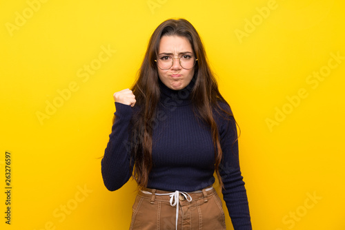 Teenager girl over isolated yellow wall with angry gesture © luismolinero