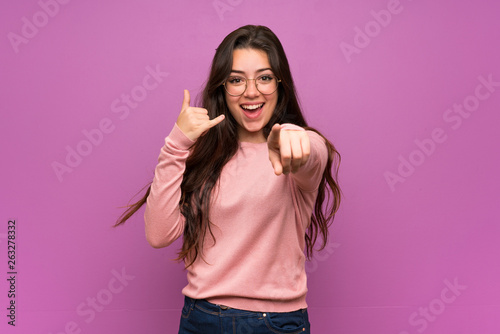 Teenager girl over purple wall making phone gesture and pointing front
