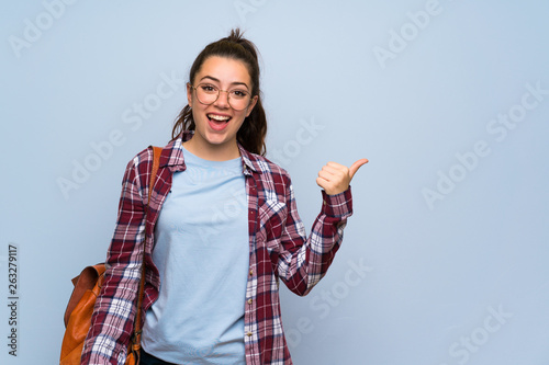 Teenager student girl over isolated blue wall pointing to the side to present a product photo
