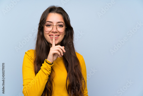 Teenager girl over isolated blue wall doing silence gesture photo