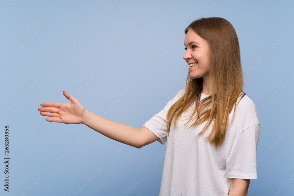 Young woman over blue wall handshaking after good deal Young woman over blue wall handshaking after good deal