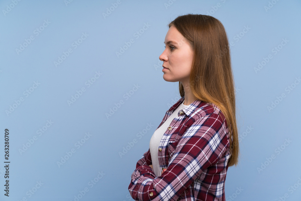 Young woman over blue wall keeping arms crossed and looking side Young woman over blue wall keeping arms crossed and looking side
