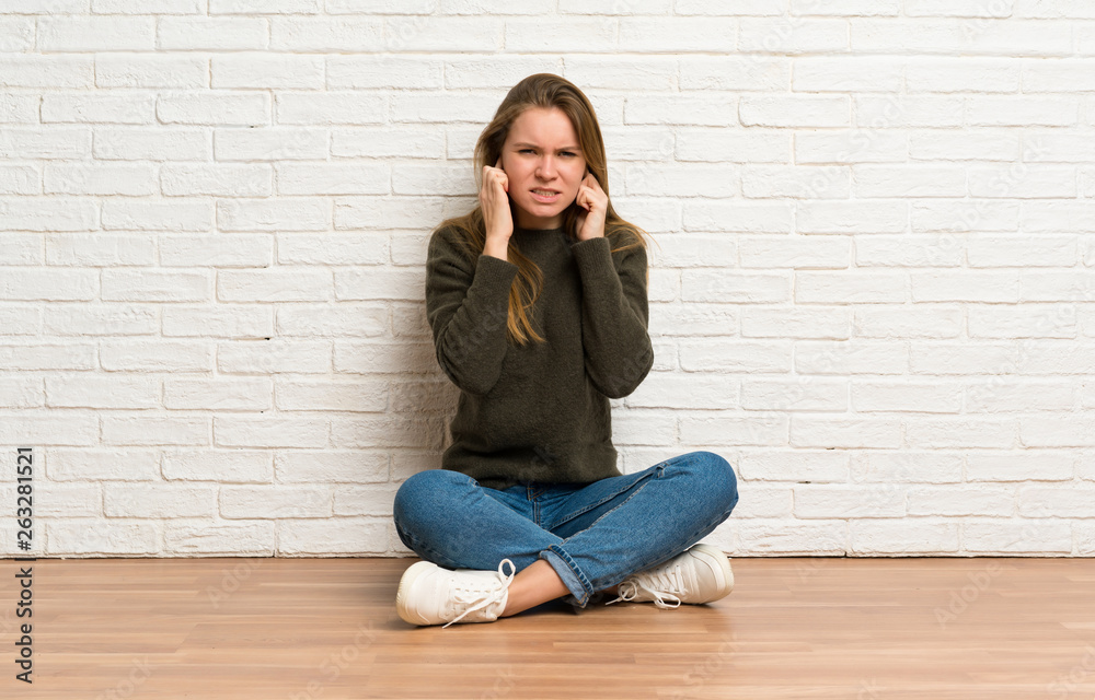Young woman sitting on the floor frustrated and covering ears Young woman sitting on the floor frustrated and covering ears