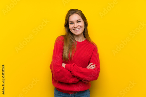 Young woman over yellow wall keeping the arms crossed in frontal position