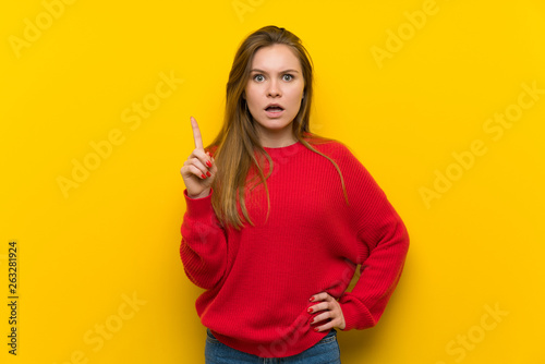 Young woman over yellow wall thinking an idea pointing the finger up