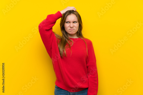 Young woman over yellow wall having doubts while scratching head photo