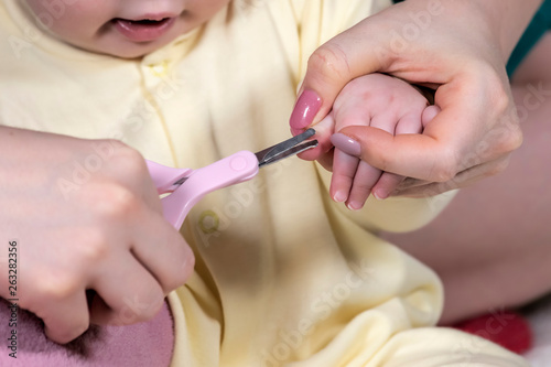 Mother cuts .her small child fingernails with protected scissors. Close-up.
