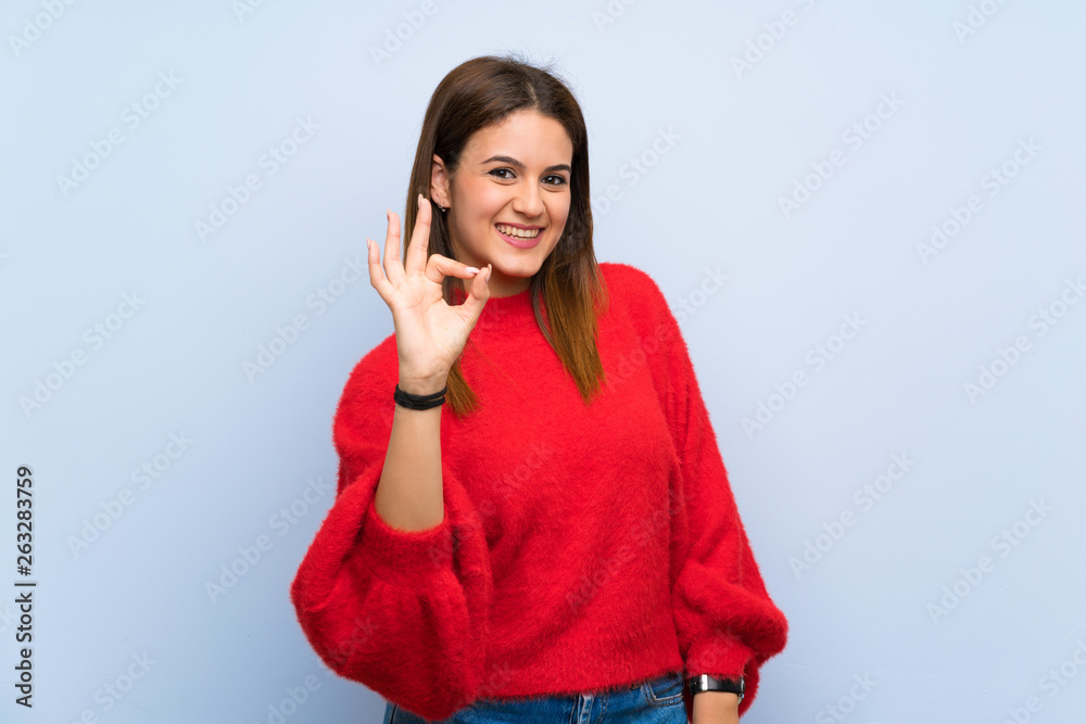 Young woman over isolated blue wall showing ok sign with fingers Young woman over isolated blue wall showing ok sign with fingers