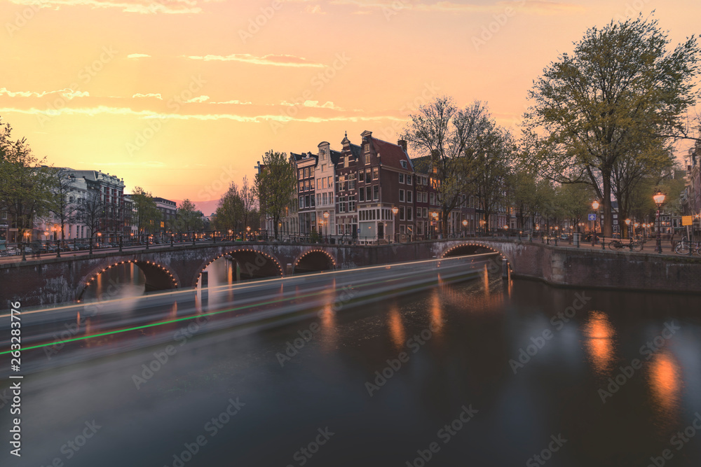 Long exposure boat cruising along the Amsterdam calm canal at the blue sunset hour, Netherlands