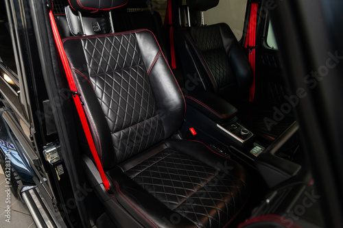 A view of a part of the interior of the car dashboard and seats from leather of black color, stitched double thread of red color with contrast stitching in a vehicle interior design workshop © Aleksandr Kondratov