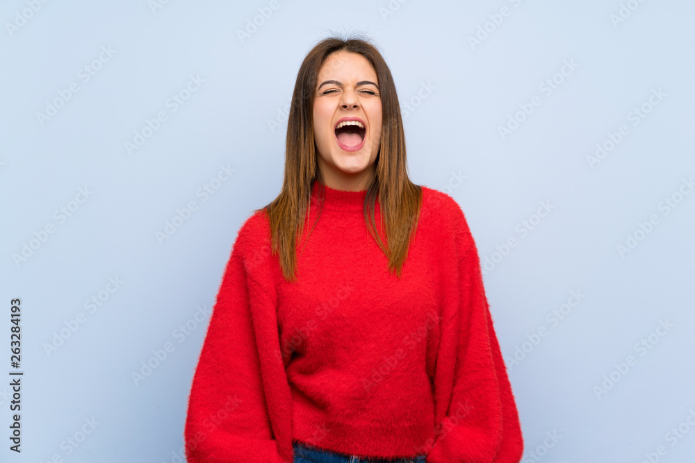 Young woman over isolated blue wall shouting to the front with mouth wide open