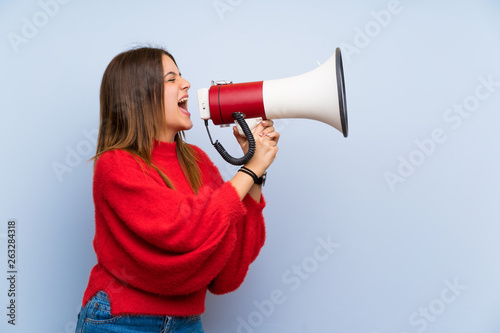 Young woman over isolated blue wall shouting through a megaphone