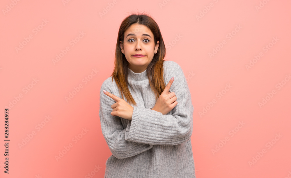 Young woman over pink wall pointing to the laterals having doubts Young woman over pink wall pointing to the laterals having doubts
