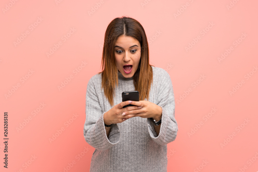 Young woman over pink wall surprised and sending a message Young woman over pink wall surprised and sending a message