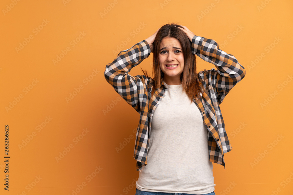 Young woman over brown wall frustrated and takes hands on head Young woman over brown wall frustrated and takes hands on head