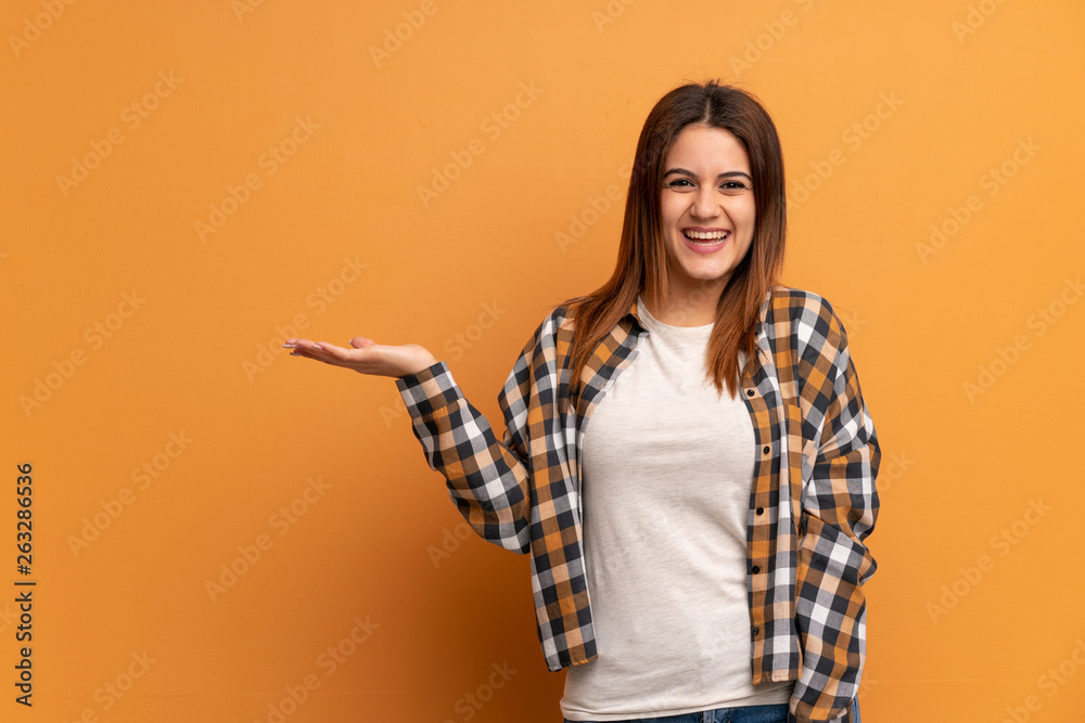 Young woman over brown wall holding copyspace imaginary on the palm to insert an ad Young woman over brown wall holding copyspace imaginary on the palm to insert an ad