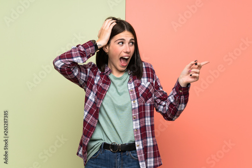 Young woman over isolated colorful wall surprised and pointing finger to the side