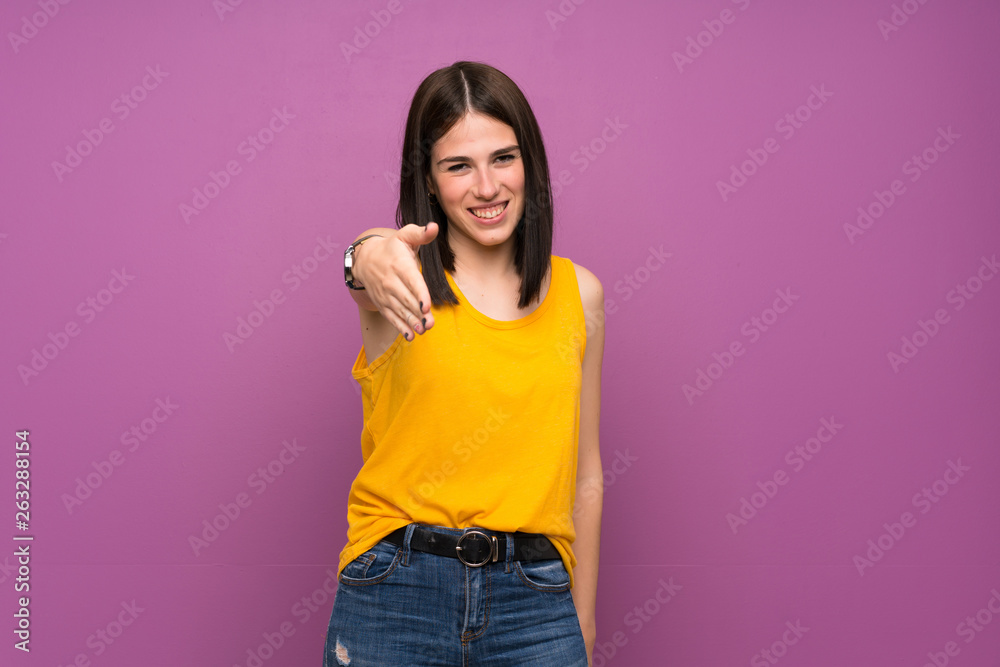 Young woman over isolated purple wall shaking hands for closing a good deal Young woman over isolated purple wall shaking hands for closing a good deal