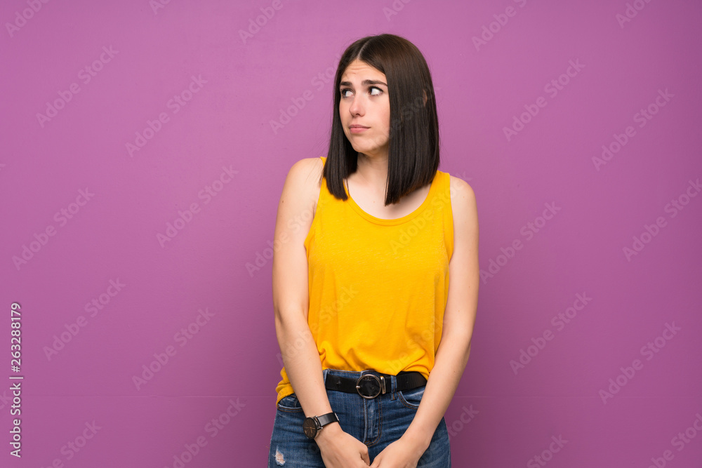 Young woman over isolated purple wall making doubts gesture looking side Young woman over isolated purple wall making doubts gesture looking side