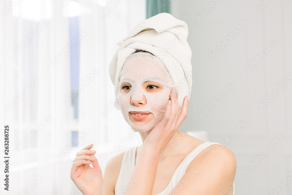 Closeup portrait of young pretty woman applying paper sheet mask on her face. Cosmetic procedure. Beauty spa and cosmetology. Closeup portrait of young pretty woman applying paper sheet mask on her face. Cosmetic procedure. Beauty spa and cosmetology.