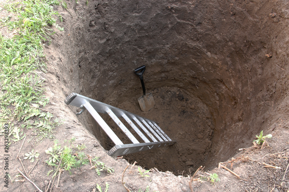 Deep pit in the ground. In the pit shovel and ladder. Digging a hole ...