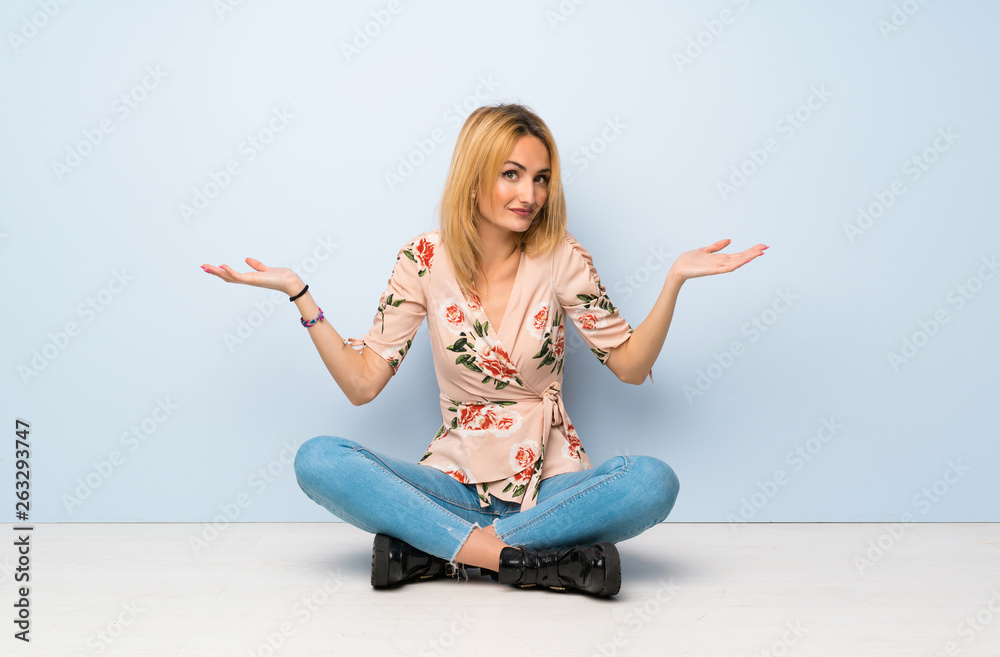 Young blonde woman sitting on the floor making doubts gesture Young blonde woman sitting on the floor making doubts gesture