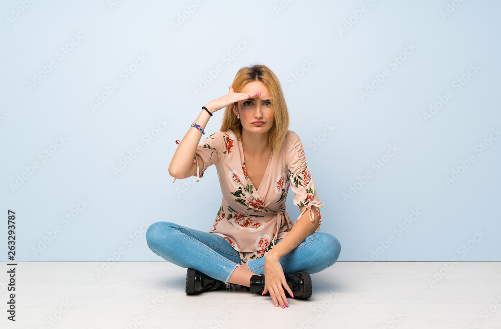 Young blonde woman sitting on the floor looking far away with hand to look something Young blonde woman sitting on the floor looking far away with hand to look something