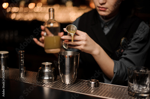 Female bartender pouring cocktail with sour mix in shaker
