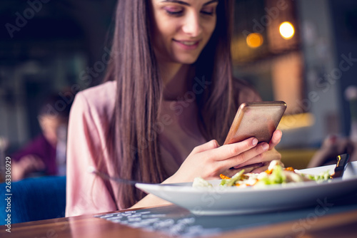 Young teenage girl checking her phone while having lunch at the restaurant