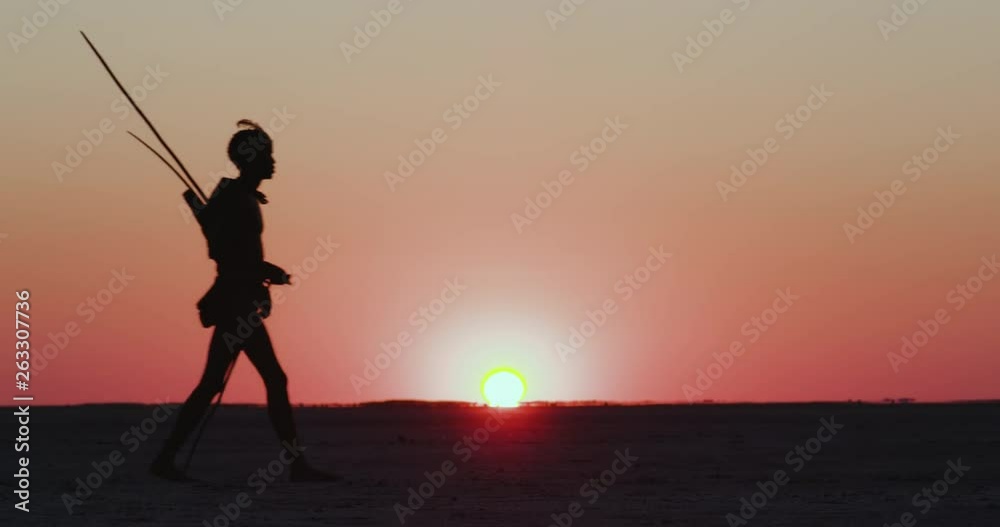 Close-up view of a group of Bushman walking on the Makgadikgadi Pans with the sun setting in the background, Botswana