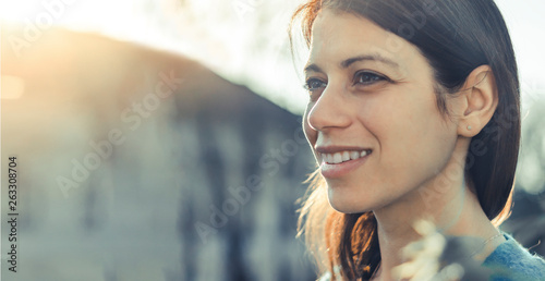 Closeup of a smiling young woman looking into the distance at sunset.