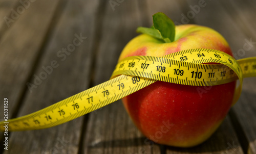 Fotografi roter apfel auf einem holztisch mit einem maßband darum