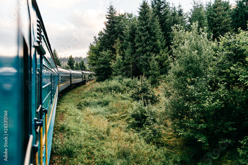 Landscape beautiful view out of window from riding train among summer nature with hills, mountains and forest. Vacation and travel concept. Locomotive with train cars moving along railroad track.