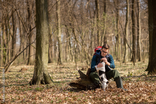 Young man with backpack hiking in the forest with his dog. Nature and physical exercise concept