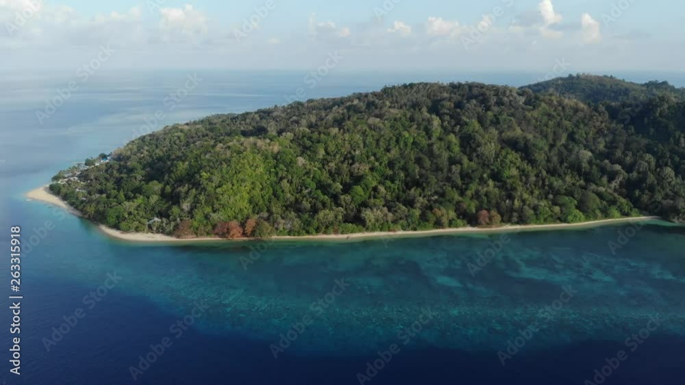 Aerial: flying over tropical Hatta island white sand beach Banda Islands Maluku Indonesia lush green forest turquoise water coral reef scenic travel destination. Native cinelike D-log color profile