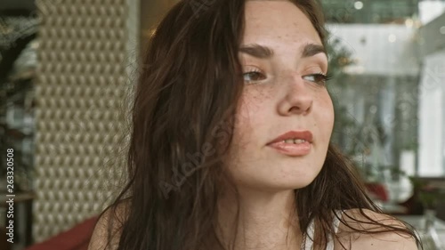 Smiling russian woman looking out while sitting in a quiet metropolitan cafe with soft natural lighting. Medium close up shot on 4k handheld