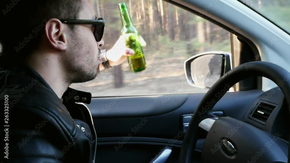 Drunk driver, man drinking beer while driving, traffic offense and accident risk, slowmotion Drunk driver, man drinking beer while driving, traffic offense and accident risk, slowmotion