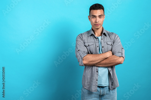 Young serios man folded his hands and standing against a blue stidio background. - Image photo