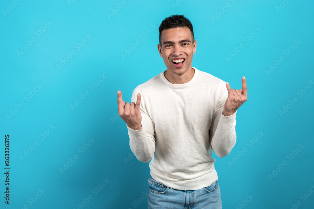 Man wearing in white shirt shouting with crazy expression doing rock symbol with hands up.  Lucky concept. - Image - obrazy, fototapety, plakaty 