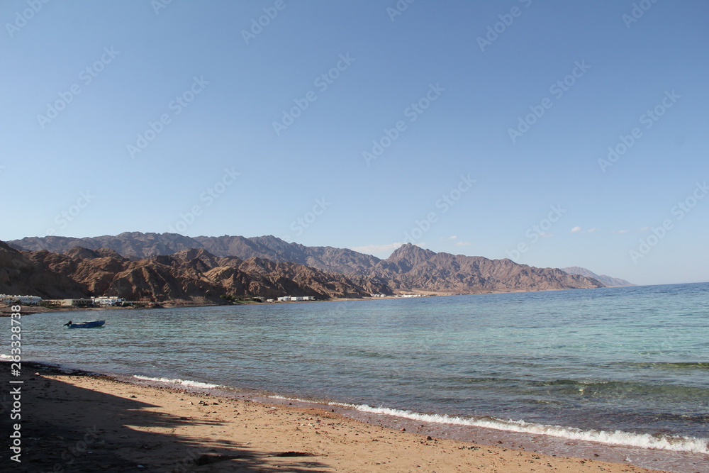 sandy seashore with a boat in the bay and mountains on the horizon