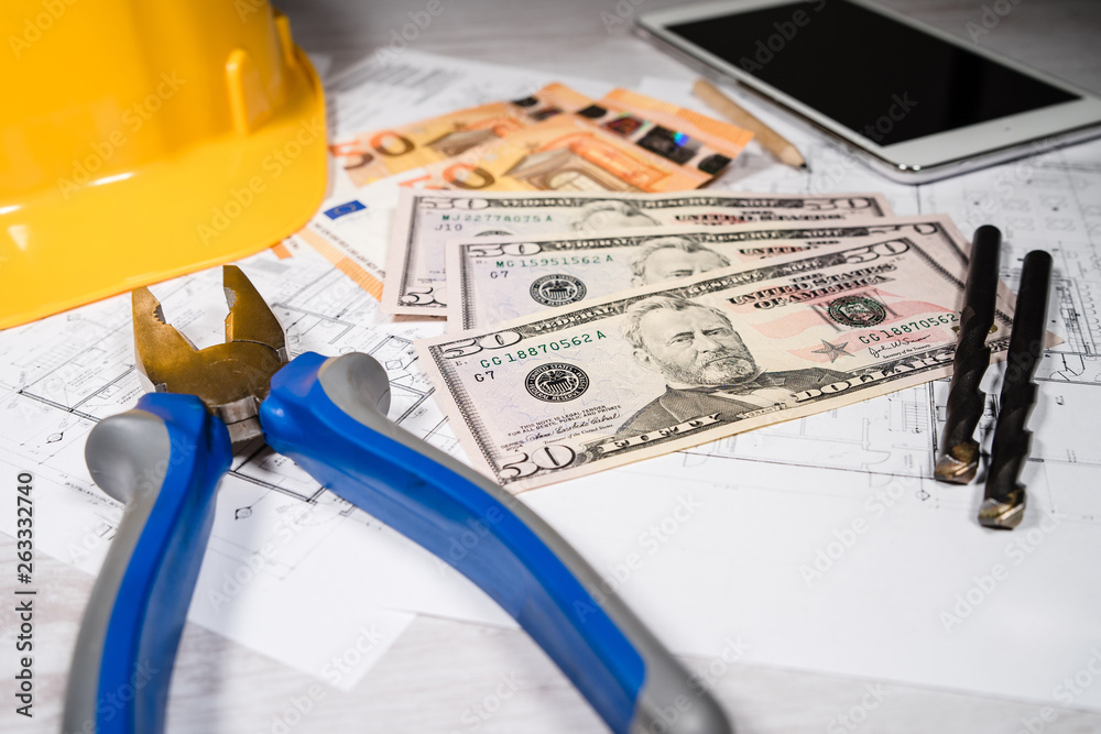Construction industry costs money banknotes us dollar euro by tools safety equipment and blueprints