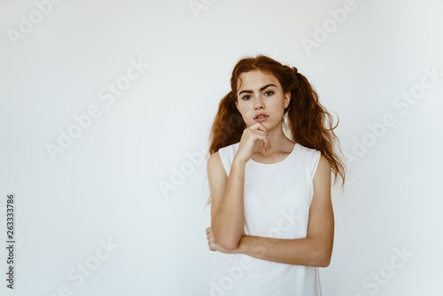 Pensive red-haired girl with ponytails on a white background. School clothes, student