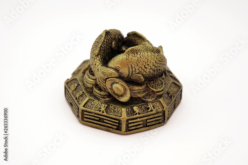 Gold sculpture of fishes on a pile of Chinese coins with good luck hieroglyphs isolated on white background. The sculpture is used in the Feng Shui art to symbolize abundance, wealth and ward.