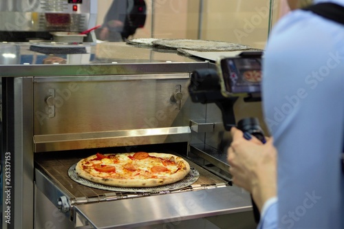 Ready Italian pizza on thin dough, fresh from the oven, production equipment. orerator shoots video production. 