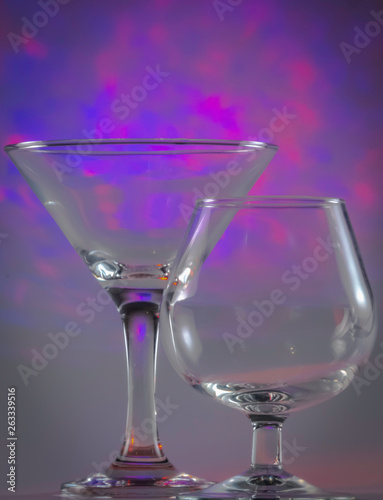Martini Glass together with Cognac Glass with flashing bright violet lights on background