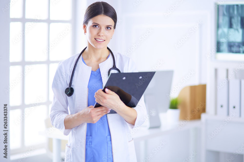 Young smiling female doctor with stethoscope holding a folder at a hospital's consulting room Young smiling female doctor with stethoscope holding a folder at a hospital's consulting room
