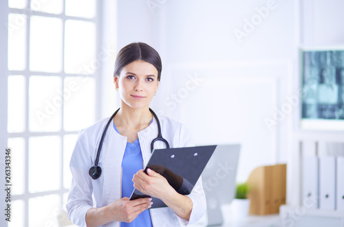 Young smiling female doctor with stethoscope holding a folder at a hospital's consulting room